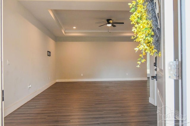 empty room with a raised ceiling, ceiling fan, and dark hardwood / wood-style flooring