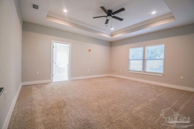 carpeted spare room with a tray ceiling and ceiling fan