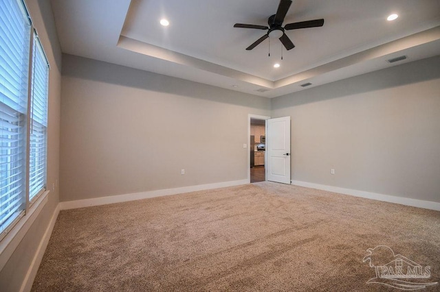 carpeted empty room with a tray ceiling, a wealth of natural light, and ceiling fan