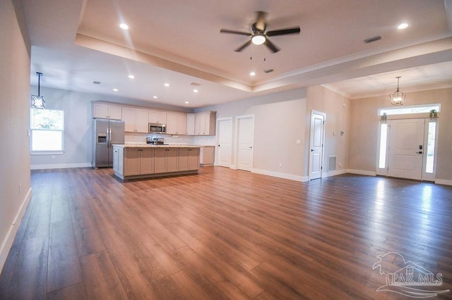 unfurnished living room with dark hardwood / wood-style floors, ornamental molding, ceiling fan with notable chandelier, and a tray ceiling