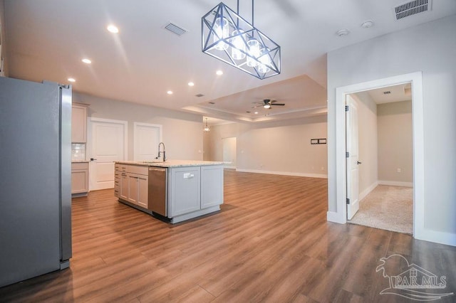 kitchen with stainless steel appliances, ceiling fan, a center island with sink, light hardwood / wood-style floors, and hanging light fixtures