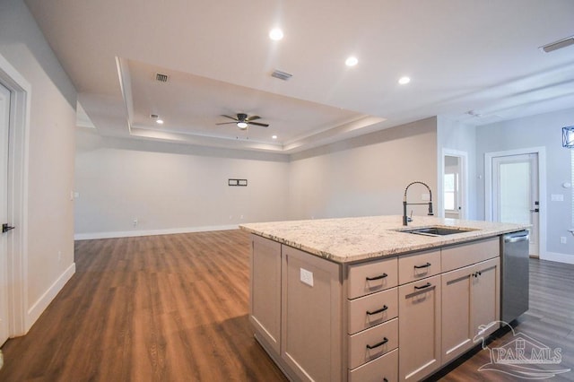 kitchen with ceiling fan, sink, dark hardwood / wood-style floors, a tray ceiling, and a center island with sink