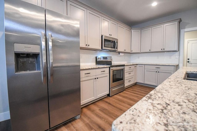 kitchen with light stone countertops, appliances with stainless steel finishes, dark hardwood / wood-style floors, and gray cabinetry