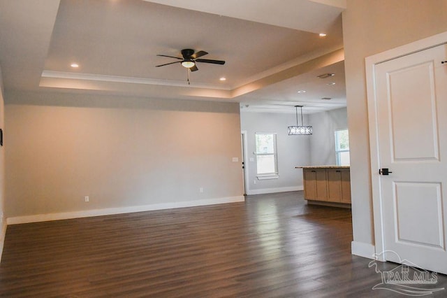 empty room featuring a raised ceiling, ceiling fan, and dark wood-type flooring