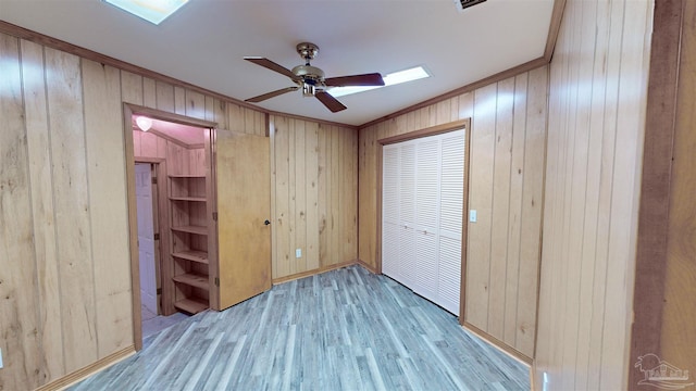 unfurnished bedroom featuring ceiling fan, wood walls, light wood-type flooring, and crown molding