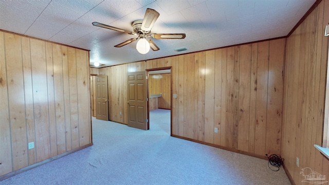 unfurnished room featuring wood walls, ceiling fan, and light colored carpet