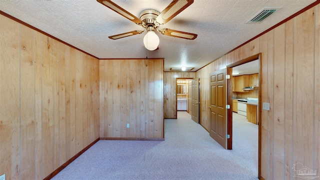 spare room featuring ceiling fan, wooden walls, light colored carpet, and a textured ceiling