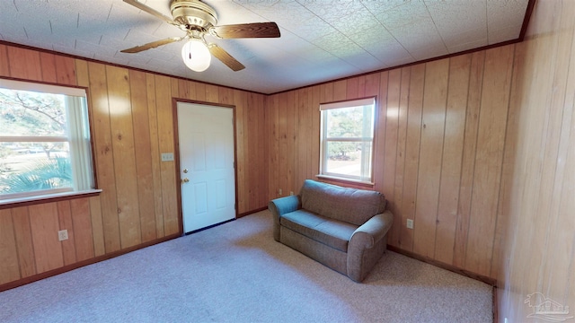 living area with a wealth of natural light, ceiling fan, light colored carpet, and wood walls