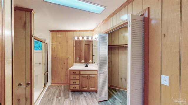 bathroom with vanity, wood walls, crown molding, hardwood / wood-style flooring, and a shower with shower door