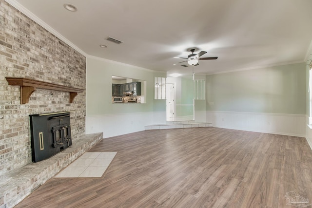 unfurnished living room with wood finished floors, visible vents, a wainscoted wall, and ceiling fan