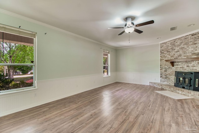 unfurnished living room with a wainscoted wall, visible vents, wood finished floors, ceiling fan, and a fireplace