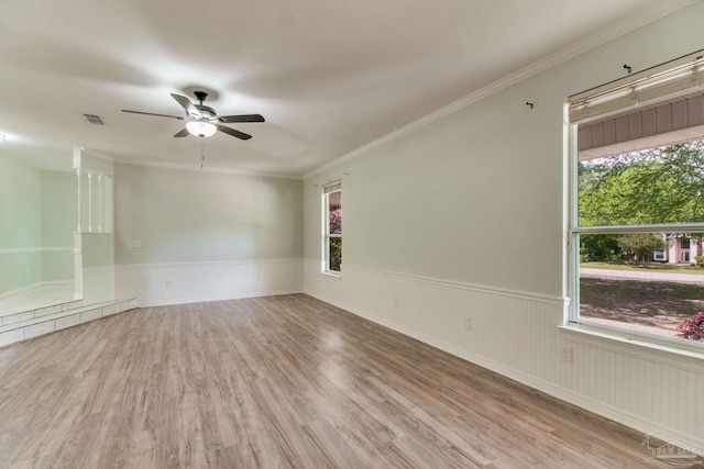 empty room with plenty of natural light, a ceiling fan, wood finished floors, and a wainscoted wall