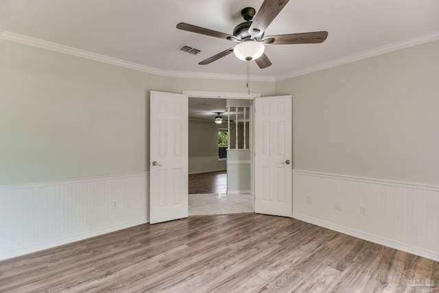 spare room with a ceiling fan, wood finished floors, a wainscoted wall, ornamental molding, and visible vents