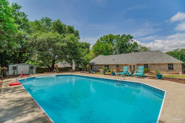 view of swimming pool featuring a storage unit, a fenced in pool, fence, a patio area, and an outdoor structure