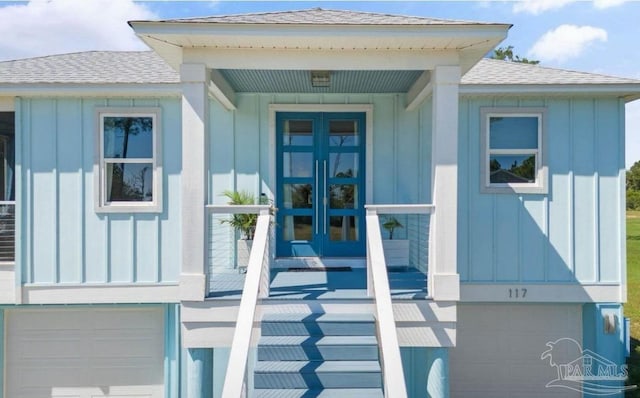 entrance to property with a garage, roof with shingles, french doors, and board and batten siding