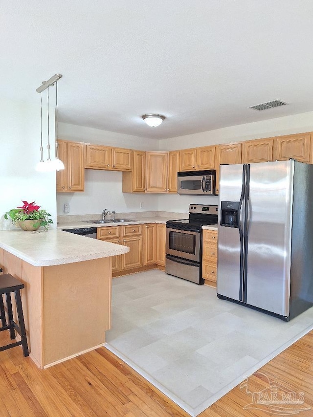 kitchen featuring a kitchen bar, sink, hanging light fixtures, kitchen peninsula, and stainless steel appliances