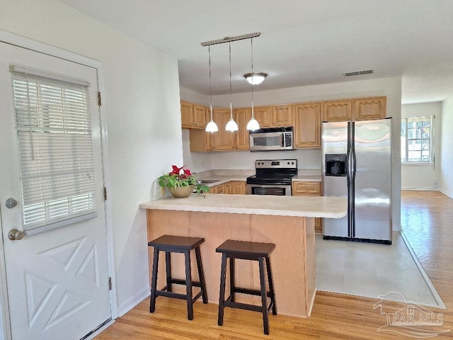 kitchen featuring decorative light fixtures, a kitchen breakfast bar, kitchen peninsula, stainless steel appliances, and light hardwood / wood-style flooring