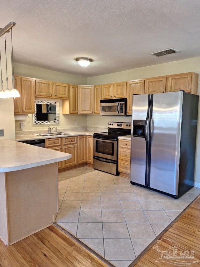 kitchen featuring pendant lighting, sink, stainless steel appliances, light brown cabinets, and light wood-type flooring