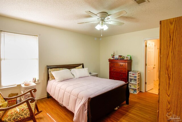 bedroom with ceiling fan, hardwood / wood-style floors, and a textured ceiling