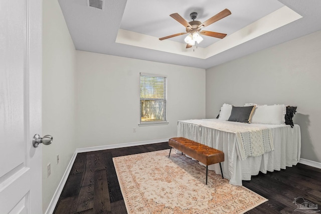 bedroom featuring dark hardwood / wood-style flooring, a tray ceiling, and ceiling fan