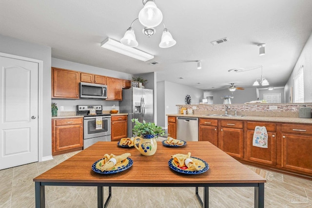 kitchen featuring pendant lighting, sink, ceiling fan, stainless steel appliances, and light stone countertops