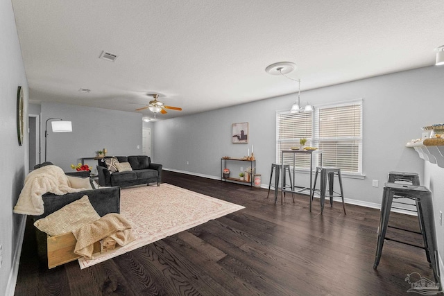 living room with dark wood-type flooring, ceiling fan with notable chandelier, and a textured ceiling