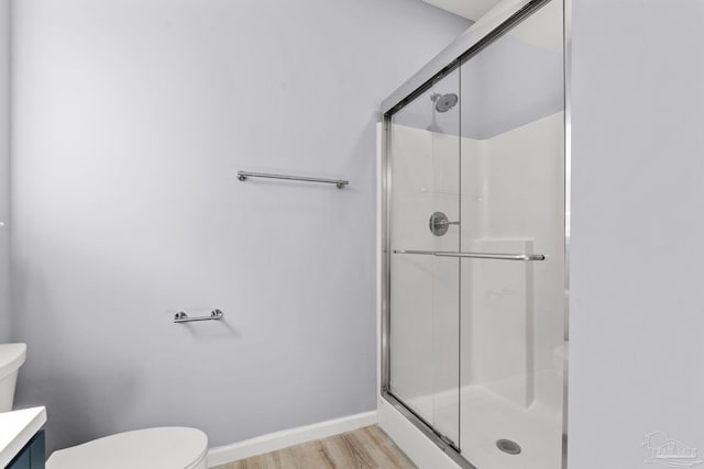 bathroom featuring a stall shower, toilet, baseboards, and wood finished floors