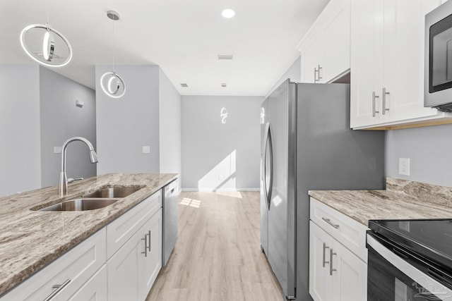 kitchen featuring a sink, light stone counters, white cabinetry, light wood-style floors, and appliances with stainless steel finishes