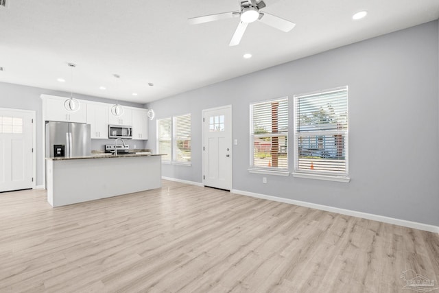 kitchen with a center island with sink, white cabinetry, stainless steel appliances, and light wood-style floors