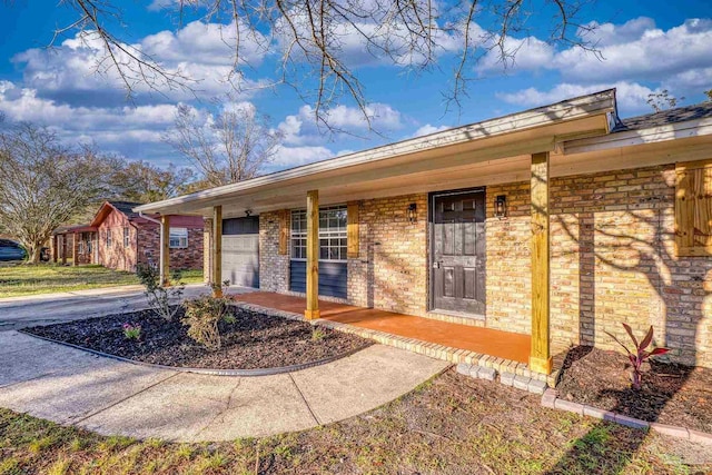 entrance to property with an attached garage, brick siding, covered porch, and driveway