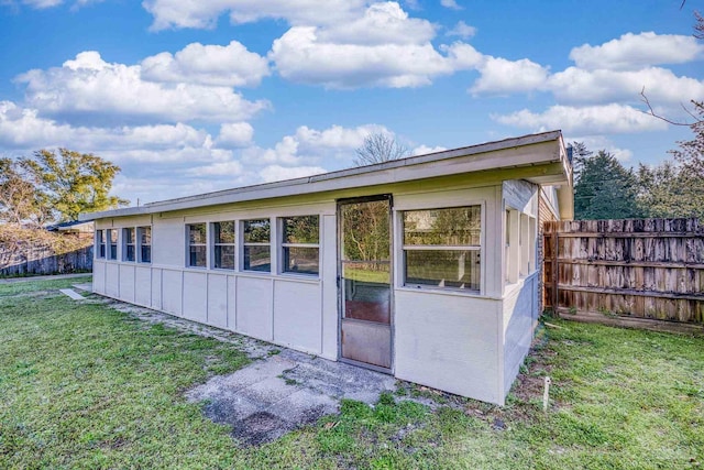 view of property exterior with board and batten siding, fence, and a lawn