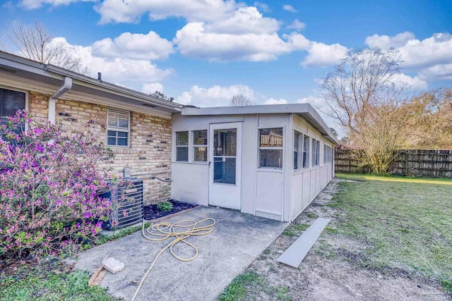 view of exterior entry with cooling unit, stone siding, a lawn, and fence