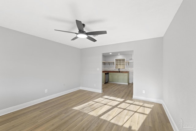 unfurnished living room with a sink, baseboards, light wood-style floors, and a ceiling fan