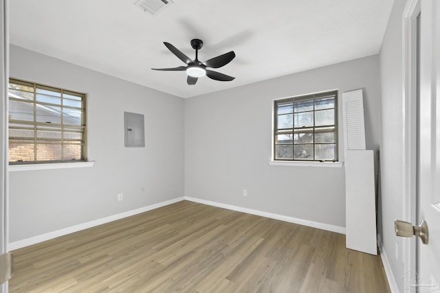 empty room with electric panel, visible vents, a healthy amount of sunlight, and wood finished floors