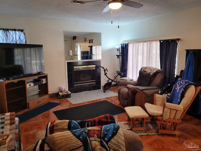 tiled living room with a tile fireplace, a textured ceiling, and ceiling fan
