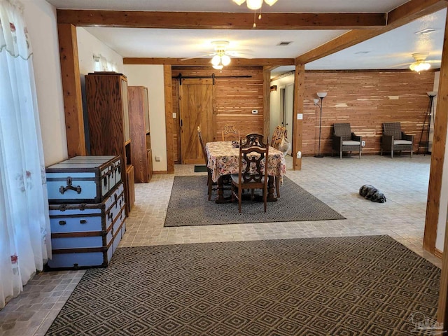 dining room featuring a barn door, ceiling fan, and wood walls