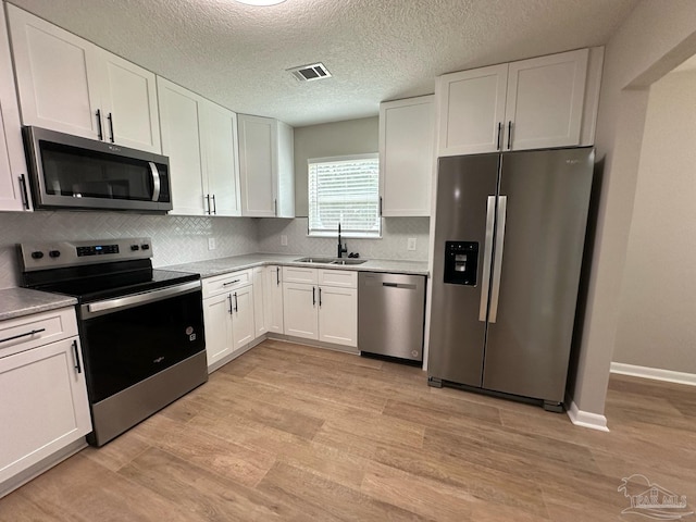 kitchen featuring stainless steel appliances, a sink, visible vents, white cabinetry, and light wood finished floors