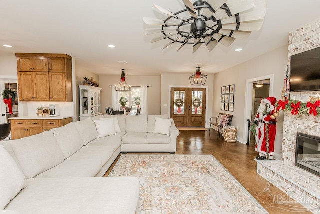 living room with french doors, ceiling fan with notable chandelier, and a brick fireplace