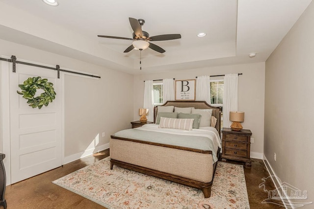 bedroom featuring ceiling fan, a barn door, and a tray ceiling