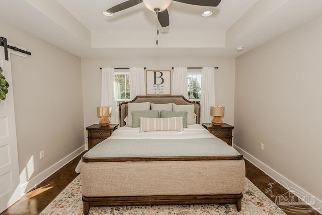 bedroom featuring a barn door, a raised ceiling, and ceiling fan