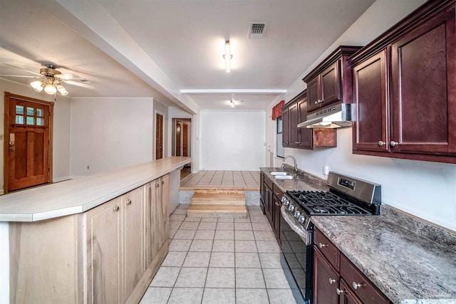 kitchen featuring stainless steel gas range oven, ceiling fan, sink, light tile patterned floors, and beamed ceiling