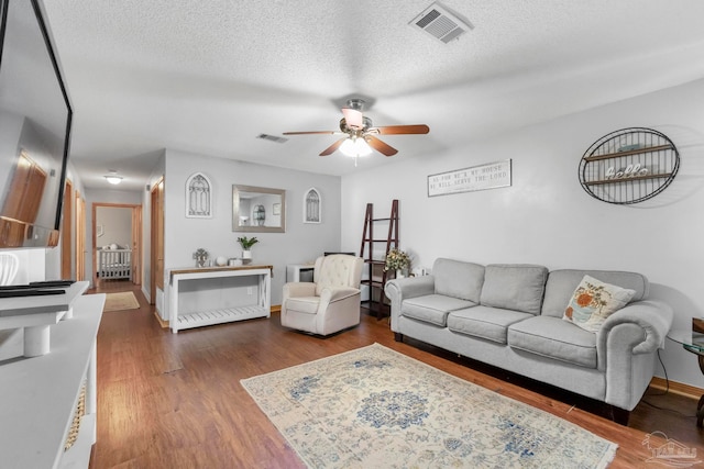 living room with a textured ceiling, dark wood-type flooring, and ceiling fan