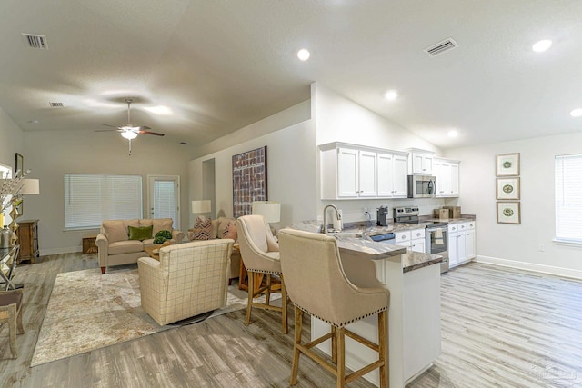 kitchen with kitchen peninsula, appliances with stainless steel finishes, light wood-type flooring, vaulted ceiling, and white cabinets