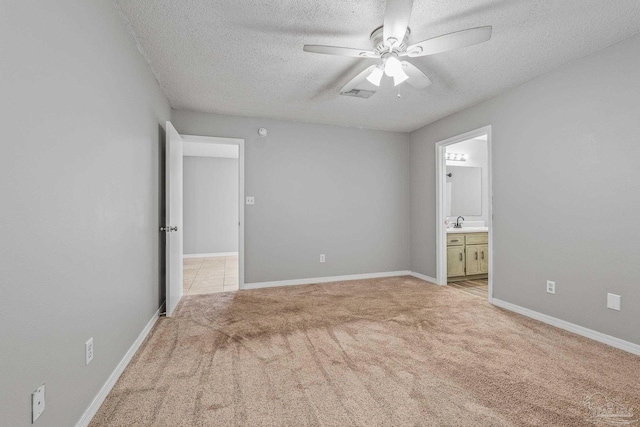 unfurnished bedroom featuring sink, light colored carpet, a textured ceiling, and ensuite bathroom