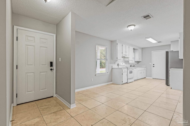 kitchen with light tile patterned floors, sink, stainless steel fridge, white range with electric cooktop, and white cabinetry