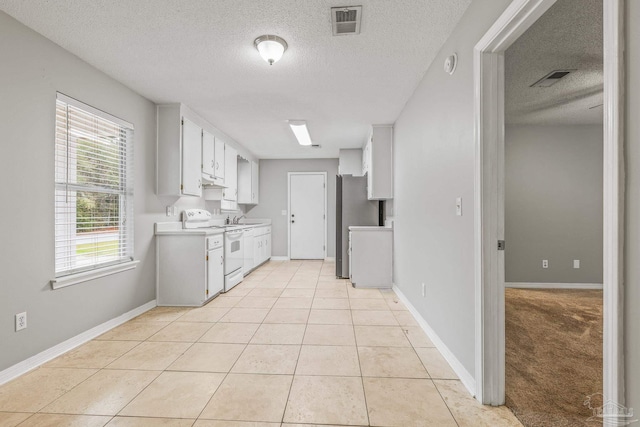 kitchen with light tile patterned floors, sink, stainless steel refrigerator, white cabinets, and white electric stove