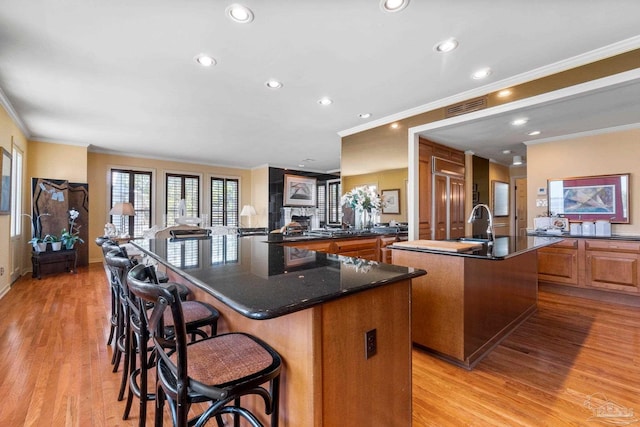 kitchen featuring a kitchen bar, ornamental molding, light hardwood / wood-style flooring, dark stone countertops, and a large island