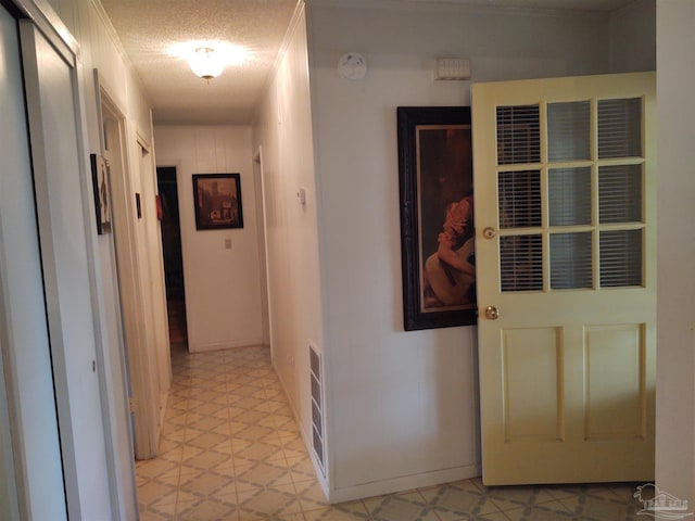 corridor featuring a textured ceiling, baseboards, visible vents, and light floors