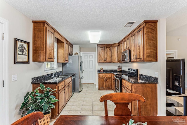 kitchen featuring brown cabinetry, visible vents, dark stone counters, light tile patterned flooring, and appliances with stainless steel finishes