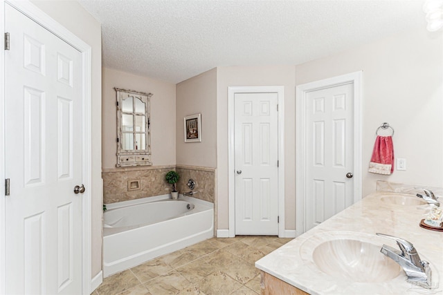 full bathroom with a sink, a garden tub, a textured ceiling, and double vanity